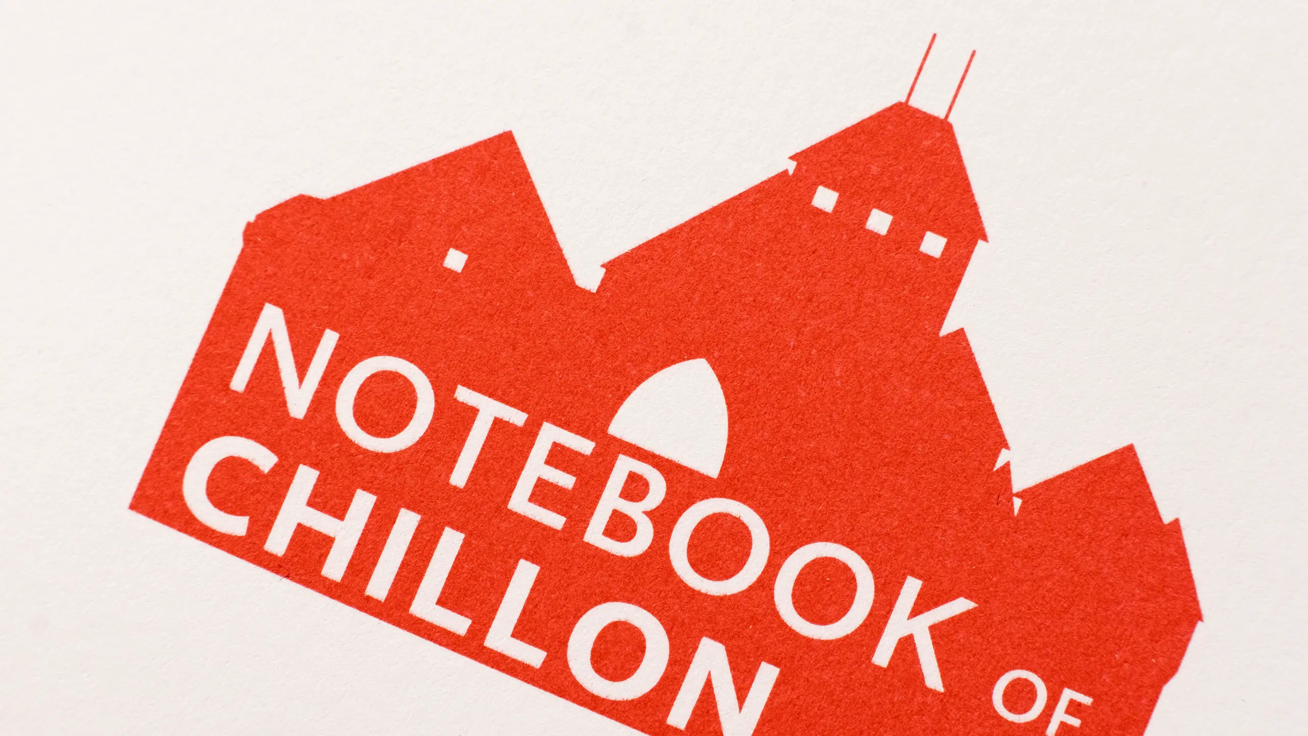 Gros plan du logo « Notebook of Chillon » imprimé en rouge, silhouette stylisée du château