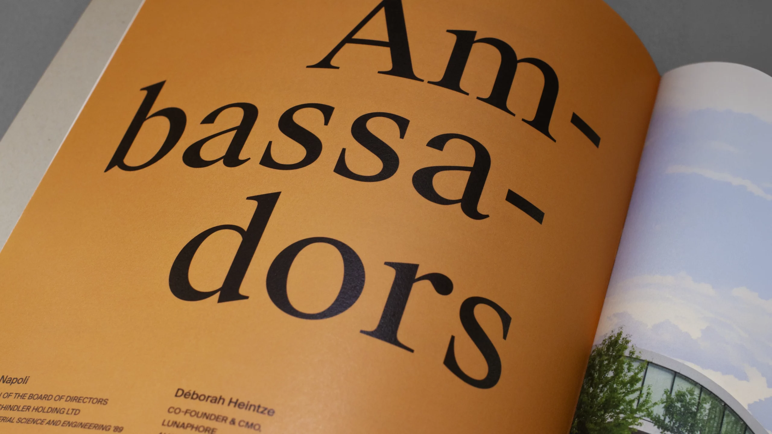 Gros plan de la page «Ambassadors» imprimée en noir sur un aplat ocre, la page illustrée suivante en train d'être tournée.