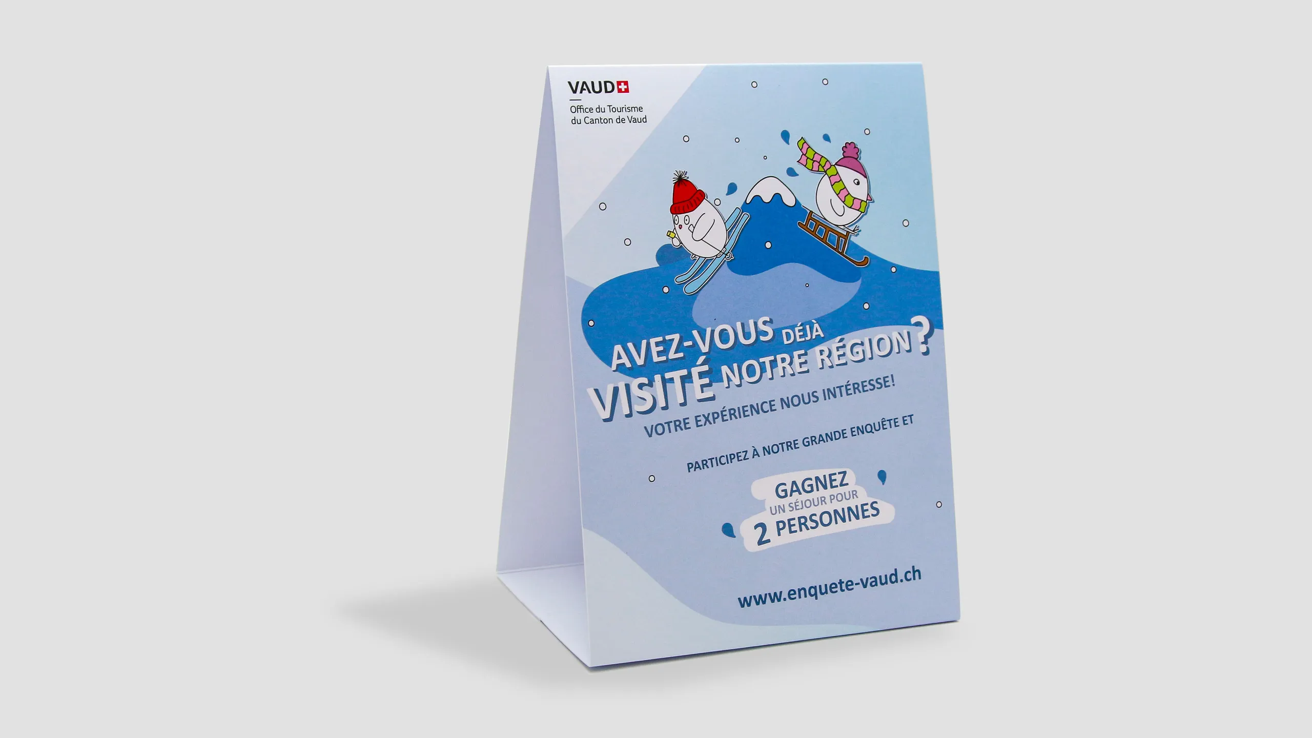 Chevalet de table bleu de l'Office du Tourisme du Canton de Vaud (français), personnages à ski et en luge, invitation à participer à l'enquête et à gagner un séjour.