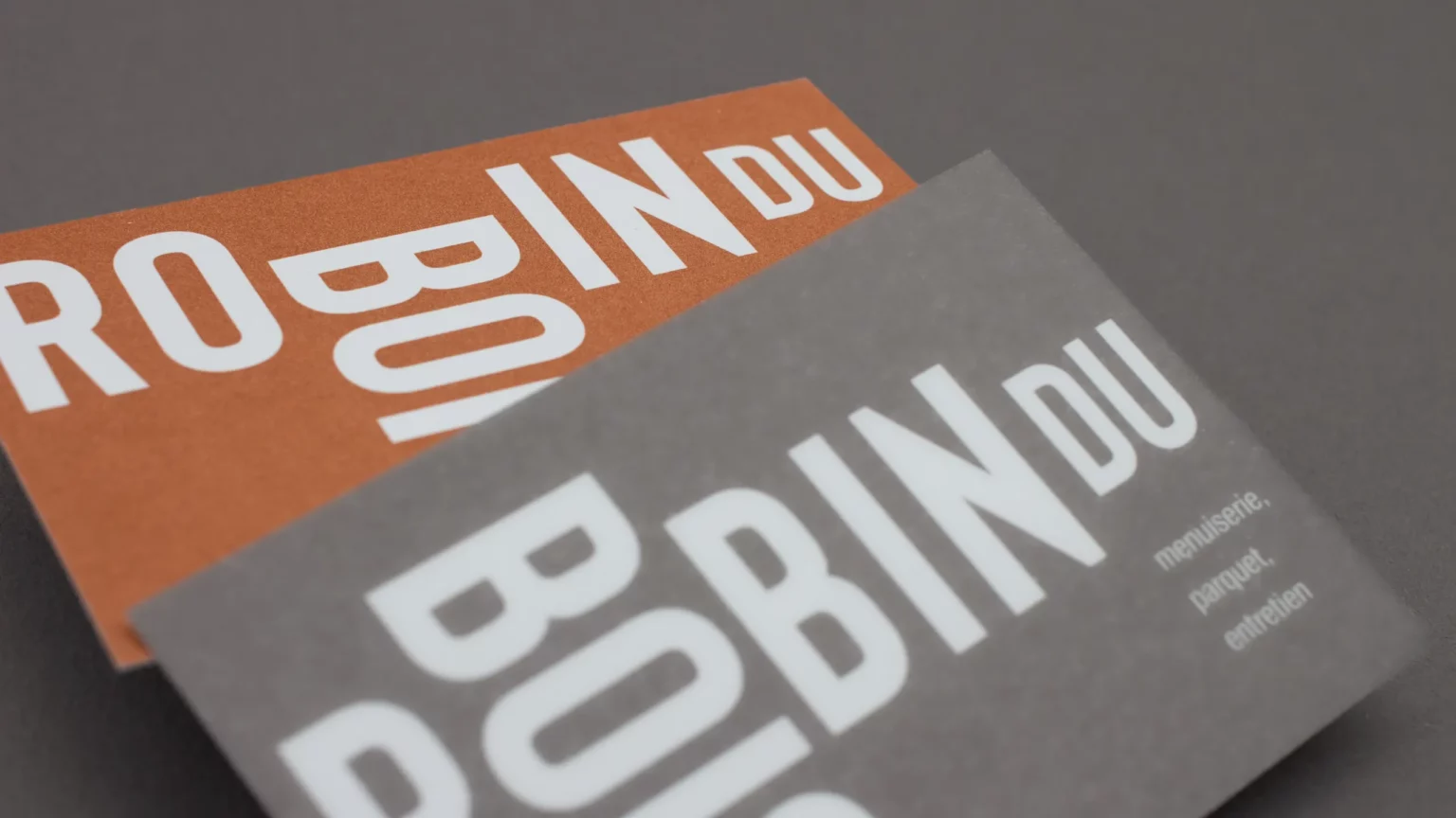 Deux cartes de visite Robin du Bois, orange et grise, où les lettres blanches du logo s’agencent autrement